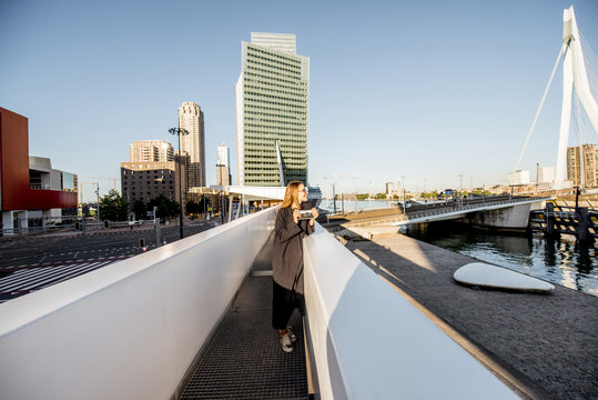 Young woman tourist standing on the bridge on the beautiful morning cityscape background in Rotterdam
