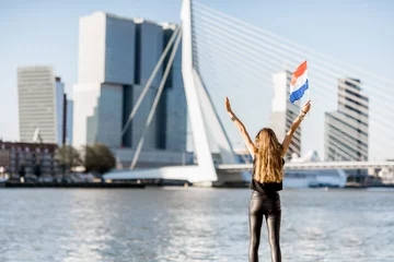 Wandaufkleber Frau mit niederländischer Flagge, die morgens in Rotterdam einen schönen Blick auf das Stadtbild am modernen Flussufer genießt © rh2010