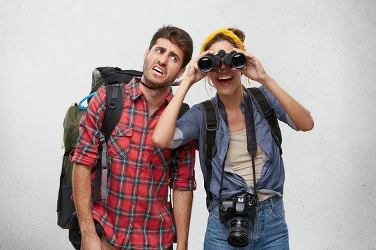 Picture of tired bearded man tourist carrying heavy backpack and cheerful excited girl with photo camera looking for place for camping using binocular during hiking trip together. People and adventure