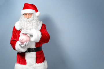 Fototapeta na wymiar Santa Claus holding piggy bang on light background