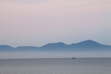 Fototapeta na wymiar Misty dusk seascape with hills on he horizon in cua dai beach, Vietnam.