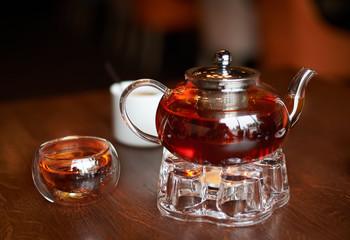 Glass infuser teapot with tea on the trivet and tea cup