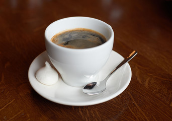 White cup with coffee, tea spoon and small cake