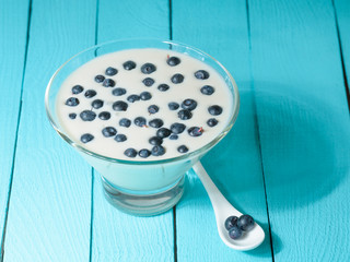 Yogurt with blueberries in a glass container stands on a wooden table.
