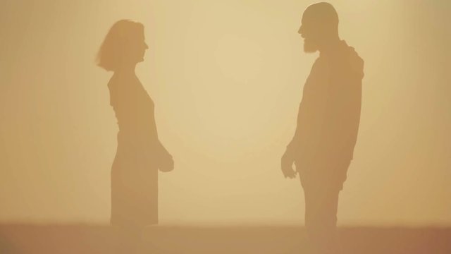 Young beautiful couple at sunset quarrels being reconciled. Man and woman in the field at sunset of the day solve problems.
