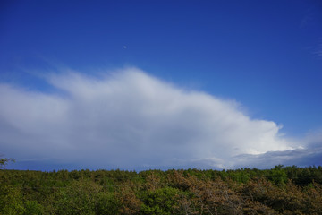 A huge fluffy cloud against the bright blue sky and moon