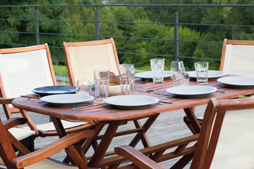 wooden garden table with white plates, cutlery and glasses against green background