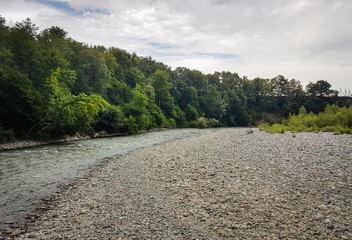 Shore of the mountain river Ashe with green trees, mountains and the sky at the background. Krasnodar region, Adygea, Russia