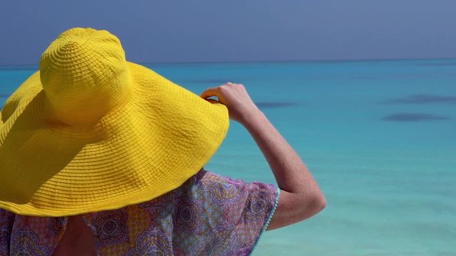 Woman in straw yellow sunhat looking to the sea on beach 