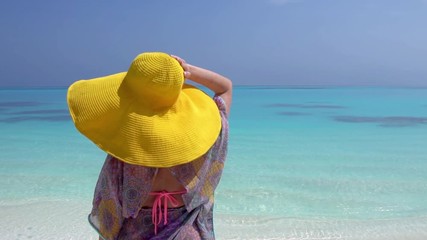 Woman in straw yellow sunhat looking to the sea on beach 