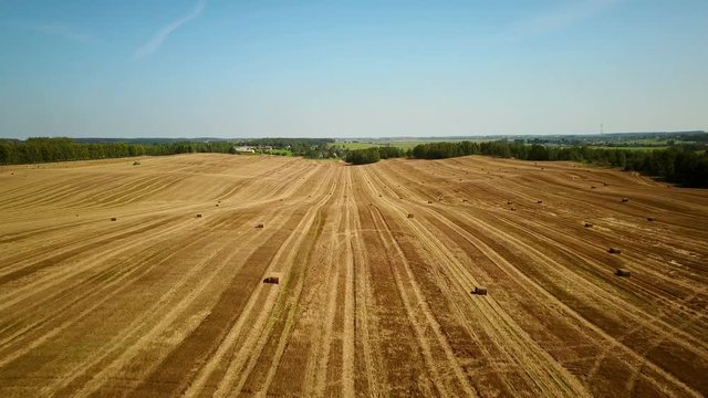 4K. Low flight over cultivated fields with haystacks after harvesting. Aerial view.