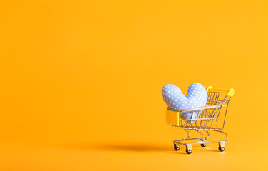 Shopping theme with shopping cart and heart shaped cushion on a yellow background