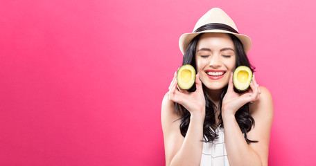 Happy young woman holding avocado halves on a pink background