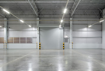 Roldeur of rolluik in fabrieks-, magazijn- of industrieel gebouw. Modern interieur met gepolijste betonnen vloer en lege ruimte voor productweergave of industriële achtergrond.