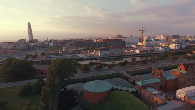 Aerial shot of Malmo Castle and city at sunset. Drone shot flying over "Malmohus" in Sweden, Turning Torso building in the background