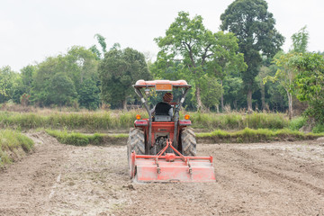 Thai farmers are using a tractor to prepare the soil for growing rice.