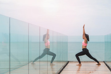 Fototapeta na wymiar Asian women play yoga on a wooden deck by the sea in the morning. With reflection in the mirror.