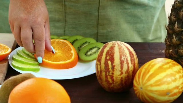 Vegetarian diet. A woman puts pieces of orange on a plate, which is on a cutting board. Hd shot with dolly from right to left.