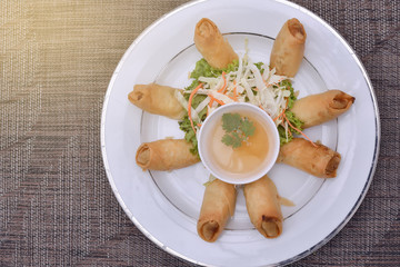 Top View Deep-fried spring rolls served with sweet and sour plum sauce on white plate, light effect.