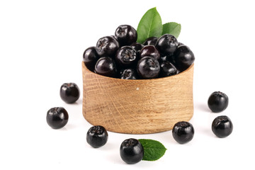 Chokeberry with leaf in wooden bowl isolated on white background. Black aronia berries