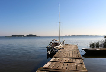 Scenic sunrise landscape with a sailing boat moored at the Sniardwy lake with Wyspa Pajecza and Czarci Ostrow islands visible in the background
