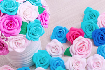 Artificial flowers roses from foam pink, blue and white, red, yellow, blue, collected in a bouquet in white pots stand on a light wooden table for decorating interiors and weddings, top view