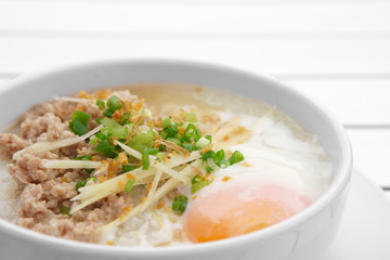 closeup pork chops rice porridge or congee with soft boiled egg and vegetable in the white bowl on the aluminium table for delicious breakfast and clean food in the morning with space