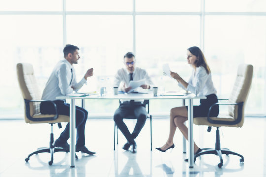 The three business people sit on the conference table