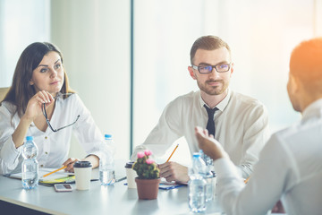 The three business people sit at the table and discuss on the sunny background