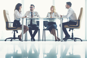 The four business people sit at the office table near the panoramic window