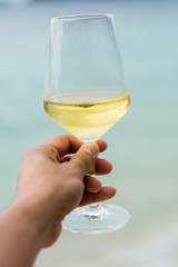 Hand holding White wine glass on beach background. Vacation and holiday travel for tourist in summer beach background.