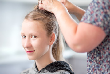 Naklejka premium ein junges, blondes Mädchen zur Vorbereitung von Jugendweihe / Konfirmation beim Friseur / Hairstyler