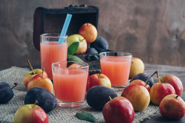 Fresh plum juice on a wooden table surrounded by fruit. In the background is a chest of fruit.