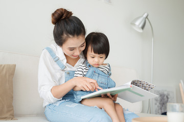 Happy loving family. Pretty young asian mother reading a book to her daughter