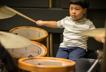 Little caucasian boy drummer playing the drum set in studio