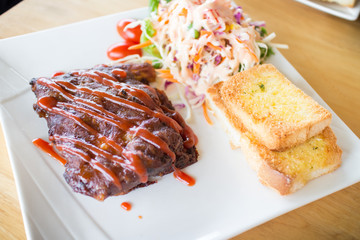 Close up view of pork barbecue ribs with barbecue sauce that served with garlic bread and vegetable salad.