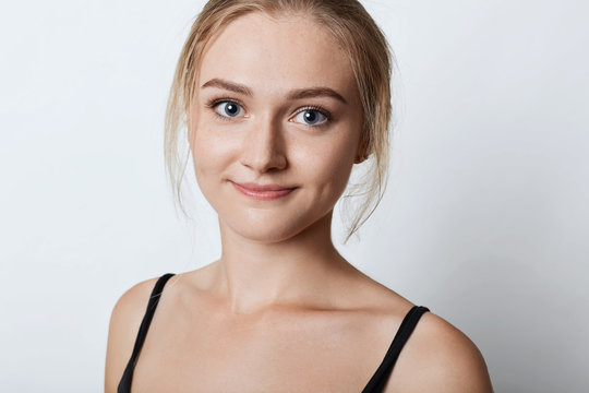 Close up portrait of attractive female with freckled skin, blue eyes and dimples on cheeks, having confident look into camera, isolated over white background. Cute blonde female posing in studio
