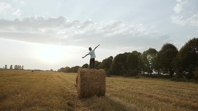 In a field on a haystack there is a boy and looks at the sunset