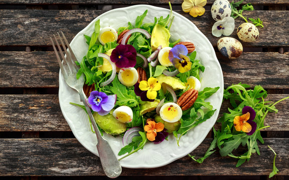 Healthy summer salad with quail eggs, avocado, pecans, wild rocket, red onion and edible viola flowers.