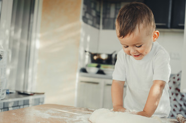 Fototapeta premium The little Boy in the kitchen hard kneads the dough