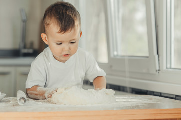 Fototapeta premium The little Boy in the kitchen hard kneads the dough