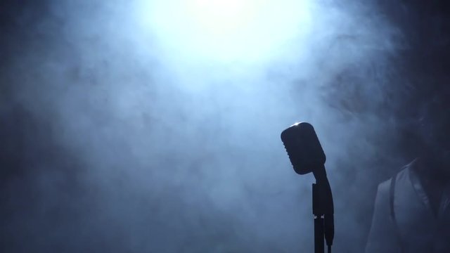 African American the darkness comes to the microphone singing in a recording studio. Black background. Silhouette. Slow motion. Close up
