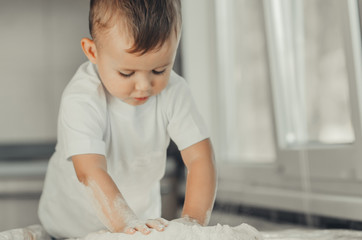 Fototapeta premium The little Boy in the kitchen hard kneads the dough