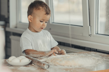 The little Boy in the kitchen hard kneads the dough