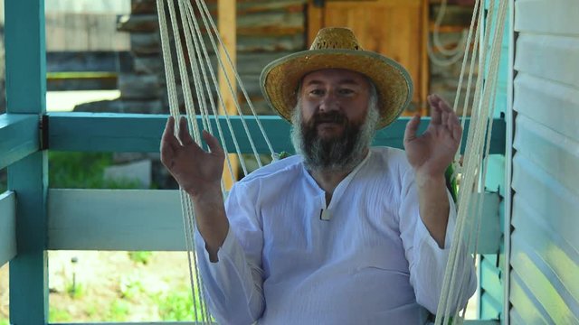Portrait of a happy farmer in a straw hat, white shirt, with a beard. Against the background of a rural landscape.