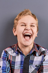 Portrait of laughing little boy. Close up studio portrait of happy joyful laughing blond hair boy. Little boy in checkered shirt laughing on grey background.