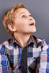 Portrait of excited little boy. Close up studio portrait of a cute little boy looking surprised on grey background. Kids facial expressions.