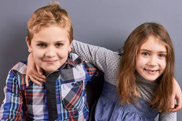 Young european brother and sister. Studio shot of cute little brother and sister embracing each other. Adorable girl and boy hugging on grey background.