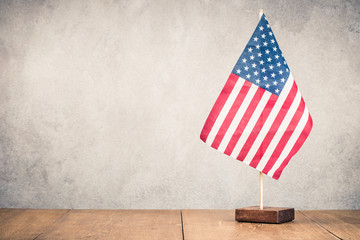 Retro USA flag on wooden table front old concrete wall background. Vintage style filtered photo