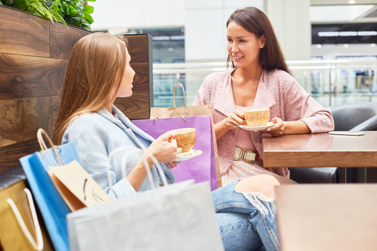 Portrait of two beautiful young women in shopping mall chatting and  drinking coffee at cafe table surrounded by paper bags